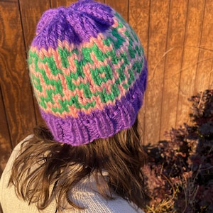 Può includere: Un berretto lavorato a mano a maglia nei toni del viola, verde e rosa. Il berretto presenta un bordo a coste e un motivo sulla corona. Realizzato in un filato morbido e strutturato, ideale per l'inverno.