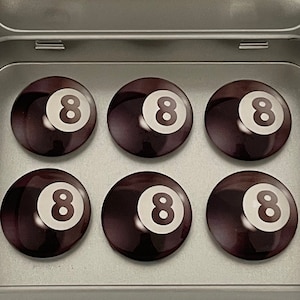 Könnte beinhalten: Ein Set mit sechs schwarzen und weißen 8-Ball-Magneten in einer silbernen Blechdose. Die Magnete sind in einem 2x3-Raster angeordnet. Die Blechdose hat ein Etikett mit dem Text "Magnet Marketplace" und der Website-Adresse "magnetmarketplace.etsy.com".