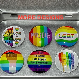 May include: A silver metal tin containing six circular magnets with various pride-themed designs. The magnets feature rainbow colors, text including "Love is Love," "PRIDE," "LGBT," and "LOVE WINS," and illustrations of a sunflower, a raised fist, and paint drips.