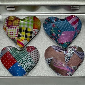 Peut inclure: Quatre aimants en forme de cœur avec des motifs patchwork à l'intérieur d'une boîte en métal argenté. Le couvercle porte une étiquette blanche avec le texte M MAGNET MARKETPLACE et magnetmarketplace.etsy.com. Chaque aimant présente un motif coloré.