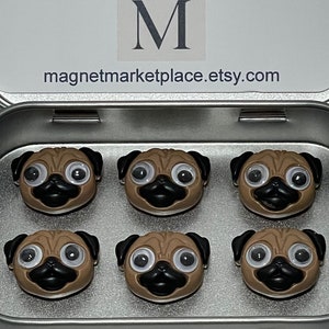 May include: A set of six small pug-shaped magnets with googly eyes, black noses, and tan faces, arranged in a silver metal tin. The inside lid features the text Magnet Marketplace and the website address magnetmarketplace.etsy.com.