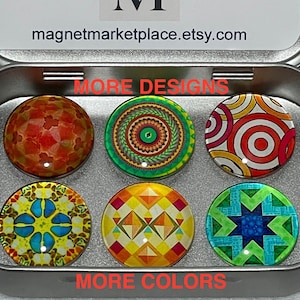 May include: A tin box with a silver lid and a white label that says "Magnet Marketplace" and "magnetmarketplace.etsy.com". The box contains six round glass magnets with colorful geometric designs. The text "More Designs" and "More Colors" is printed on the tin box.