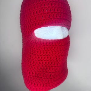 May include: Red crocheted ski mask with a white eye hole opening.