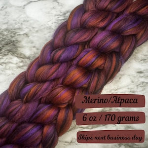 May include: Braided Merino/Alpaca yarn in shades of purple, orange, and brown. The yarn is 6 oz / 170 grams. The yarn is a blend of Merino wool and Alpaca fiber. The colors are vibrant and the texture appears soft.