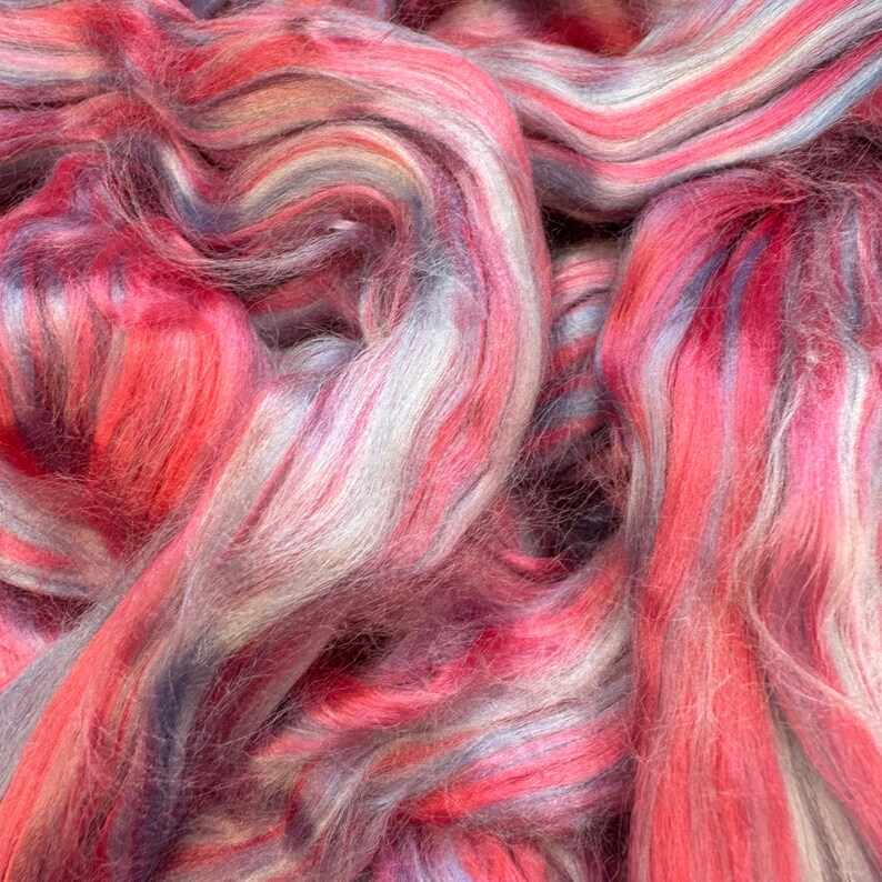 Pode incluir: Um close-up de um monte de fio colorido com tons de rosa, branco e cinza. O fio &eacute; macio e felpudo, e &eacute; perfeito para tricotar ou fazer croch&ecirc;.