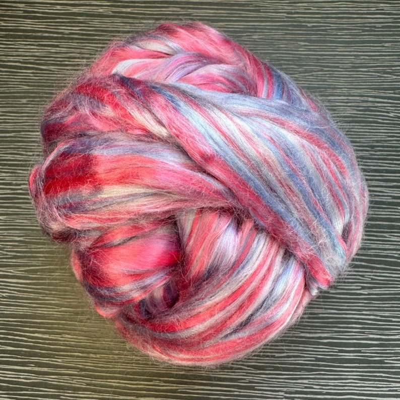 Pode incluir: Uma bola de fibra rosa, branca e azul. A fibra est&aacute; disposta em um padr&atilde;o solto e espiralado.