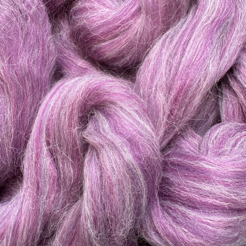 May include: A close-up of a bundle of purple and white wool roving. The wool is soft and fluffy, and it is perfect for spinning or felting.