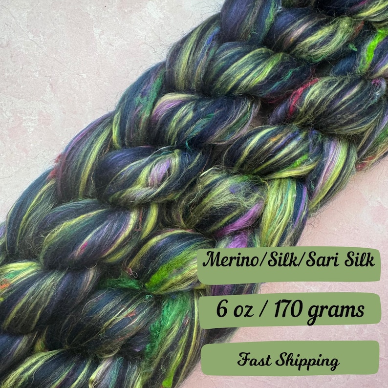 May include: A braid of black, green, and purple merino wool, silk, and sari silk yarn. The yarn is 6 ounces or 170 grams.