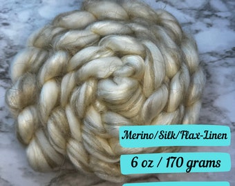 May include: A close-up of a ball of white and gray yarn, made of merino wool, silk, and flax linen. The yarn is 6 ounces or 170 grams. Merino/Silk/Flax-Linen 6 oz / 170 grams Ships next business day