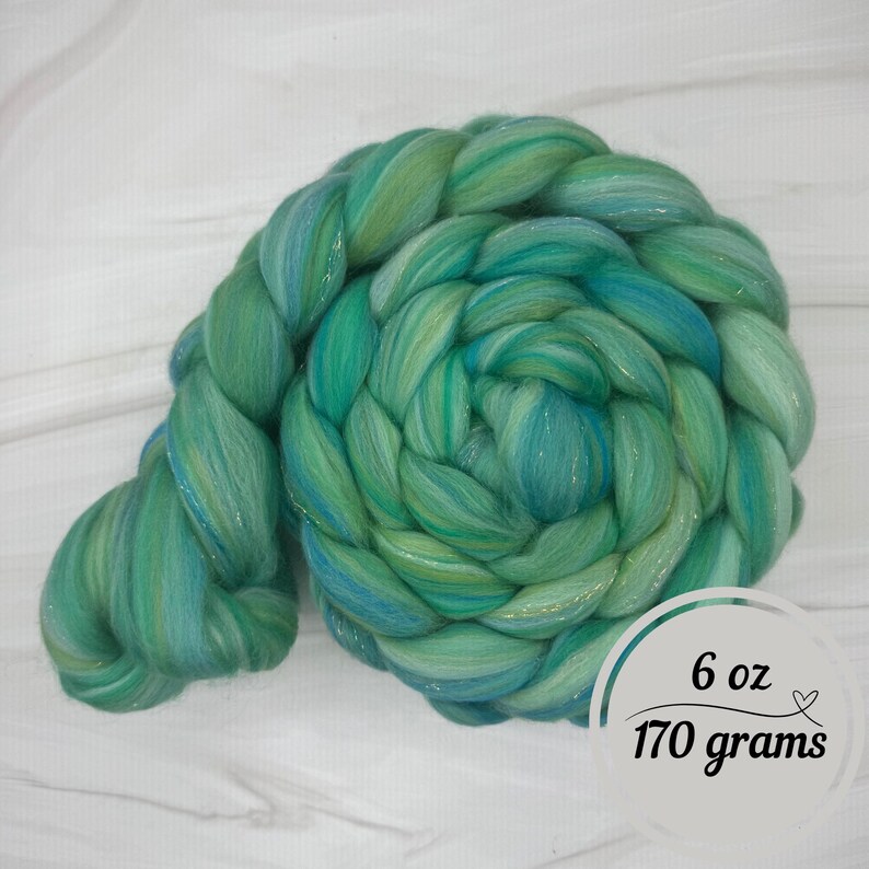 Pode incluir: Uma tran&ccedil;a vibrante de fibra tingida &agrave; m&atilde;o em tons de verde-azulado e verde. A fibra &eacute; um material macio e luxuoso, perfeito para fiar ou outras artes t&ecirc;xteis. A etiqueta indica um peso de 170 gramas (6 oz).