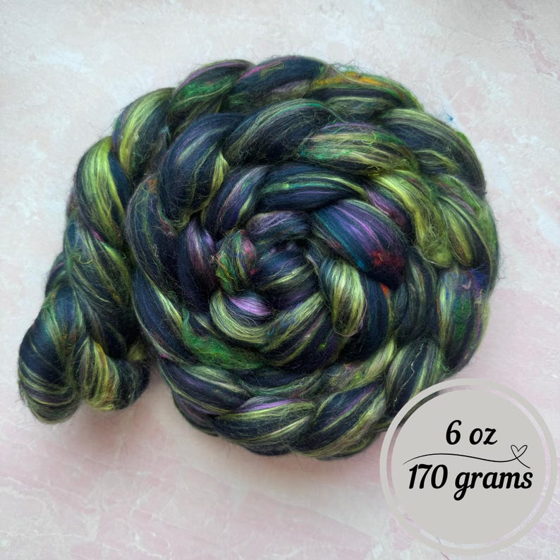 May include: A 6 ounce (170 gram) bundle of black, green, and purple fiber. The fiber is arranged in a loose braid.