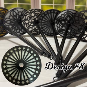 May include: A collection of black decorative bottle stoppers with intricate, laser-cut designs. The stoppers feature various patterns, including floral and geometric shapes, with a white or cream-colored backing. The text "Design #8" is visible.