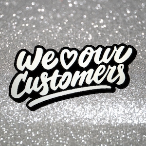 Pode incluir: Texto branco sobre fundo preto com um s&iacute;mbolo de cora&ccedil;&atilde;o que diz "We &hearts; our customers" sobre um fundo de glitter prateado.