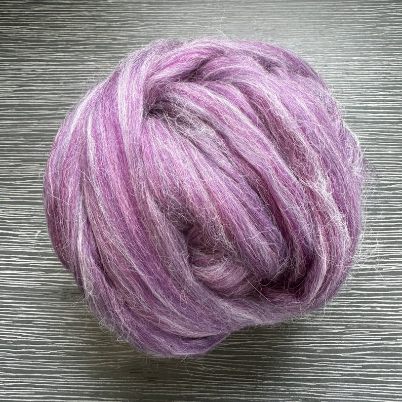 May include: A large ball of purple and white wool yarn. The yarn is soft and fluffy, and it is perfect for knitting or crocheting.