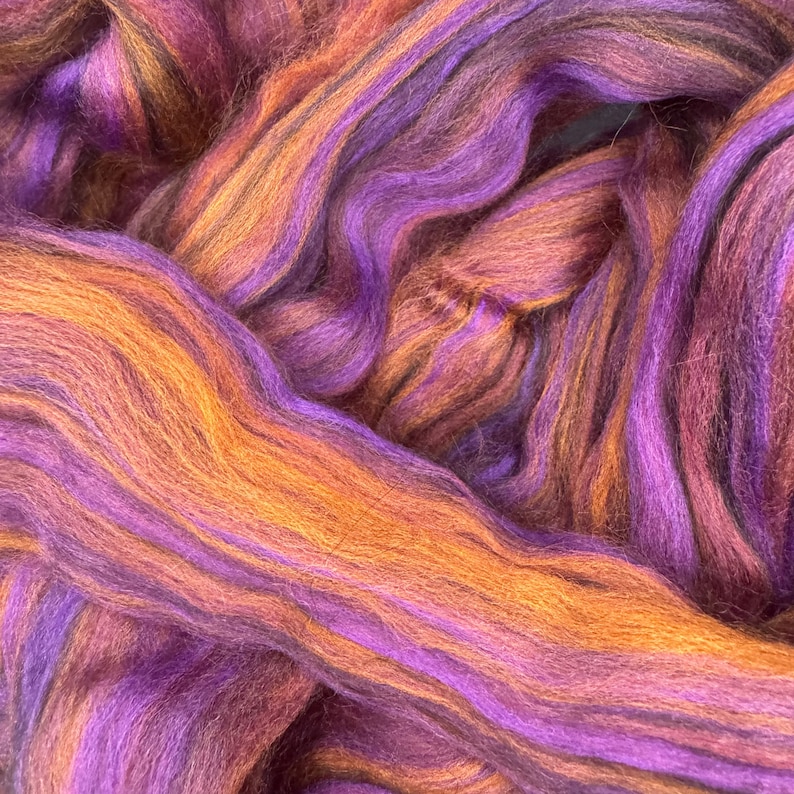 May include: Close-up of colorful fiber art. The image features strands of fiber in shades of purple, orange, and brown. The fibers are arranged in wavy patterns, creating a textured and visually appealing display. This fiber art is suitable for various craft projects.