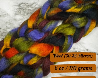 May include: A braid of wool yarn in shades of purple, green, orange, yellow, and brown. The yarn is 6 ounces or 170 grams and is made from wool that is 30-32 microns. The text "Wool (30-32 Micron)", "6 oz / 170 grams", and "Ships next business day" is visible in the image.