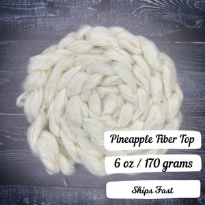May include: A cream-colored pineapple fiber top, tightly coiled and textured. The image shows the fiber top against a dark wood grain background. The text on the image reads "Pineapple Fiber Top" and "6 oz / 170 grams".