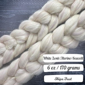 May include: Braided white Lonk/Merino/Seacell fiber, 6 oz. The fiber is a soft, off-white color, with a slightly textured appearance. The fiber is arranged in two thick, parallel braids.
