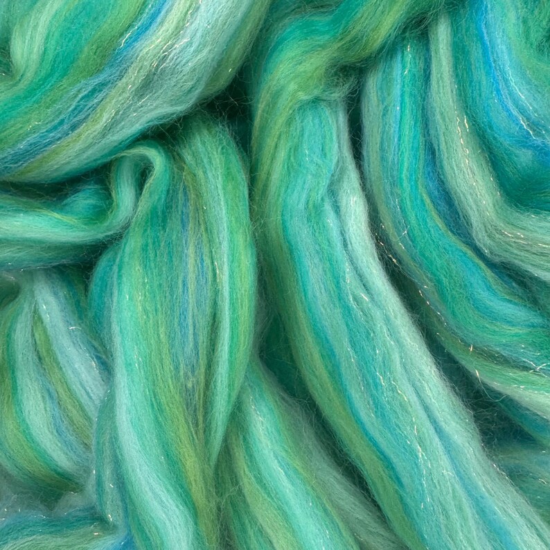 Pode incluir: Close-up de um feixe de fibra em tons de verde-azulado, turquesa e verde, com sutis reflexos prateados. As fibras s&atilde;o macias e onduladas, criando uma apar&ecirc;ncia texturizada. Ideal para projetos de artesanato como fia&ccedil;&atilde;o, feltragem ou tecelagem.
