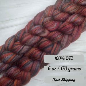 May include: Braided yarn in shades of red, orange, and gray. The yarn is labeled "100% BFL" and weighs 6 oz / 170 grams. The yarn is suitable for knitting, crocheting, or other fiber arts projects.