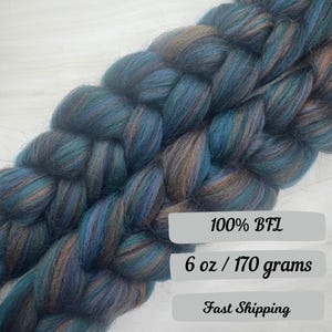 May include: Braided roving in shades of teal, blue, and brown. The fiber is labeled as 100% BFL and weighs 6 oz (170 grams). The roving is tightly twisted, showcasing the blend of colors.