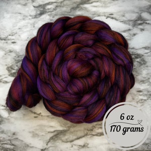 May include: A tightly coiled braid of colorful fiber in shades of deep purple, burgundy, and burnt orange. The image includes a circular graphic indicating the fiber weighs 6 oz (170 grams).