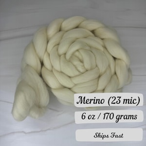 May include: A large, off-white braid of Merino wool. The text on the image reads "Merino (23 mic)" and "6 oz / 170 grams". The wool is tightly woven, and the texture is visible. The product is likely for crafting or textile projects.