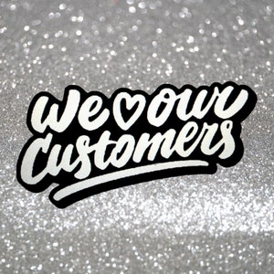 Może przedstawiać: Biały tekst na czarnym tle z symbolem serca, kt&oacute;ry brzmi "We &hearts; our customers" na tle srebrnego brokatu.
