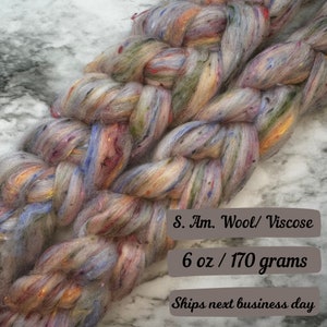May include: A pile of colorful wool and viscose yarn in shades of blue, green, orange, and red. The yarn is 6 ounces or 170 grams.