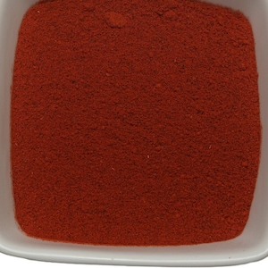 May include: A small white square bowl filled with a bright red powder. The powder is finely ground and has a smooth, even texture.
