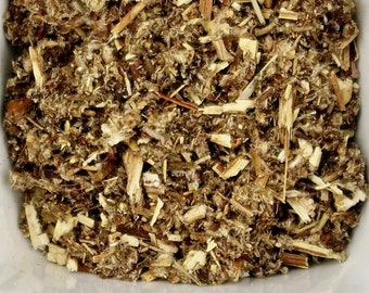 May include: A white ceramic bowl filled with dried, light brown and green herbs. The herbs are chopped into small pieces and appear to be a blend of different types.
