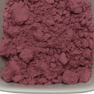 May include: A close-up view of a small white bowl filled with a fine, pink powder. The powder is evenly distributed and appears to be a natural ingredient.