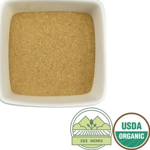 K&ouml;nnte beinhalten: Eine wei&szlig;e quadratische Schale gef&uuml;llt mit einem hellbraunen Pulver. Die Schale befindet sich auf einem wei&szlig;en Hintergrund. Der Text "USDA Organic" befindet sich auf einem gr&uuml;nen und braunen runden Aufkleber. Der Text "Zee Herbs" befindet sich auf einem gr&uuml;nen und wei&szlig;en Aufkleber mit einem Berg- und Feldmotiv.
