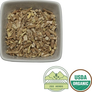 May include: A white ceramic bowl filled with dried, light brown and beige pieces of organic angelica root. The bowl is on a white background. The image also includes a green and white USDA Organic seal and a green and white Zee Herbs logo.