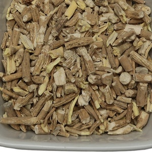 May include: A close-up view of a bowl filled with dried, light brown and beige root pieces. The pieces are irregularly shaped and have a rough texture.