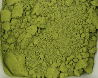 Puede incluir: Un cuenco blanco cuadrado lleno de polvo de matcha verde vibrante. El polvo tiene una textura fina, ligeramente granulada, con grumos visibles. El cuenco está sobre un fondo blanco liso, resaltando el color y la textura del matcha.