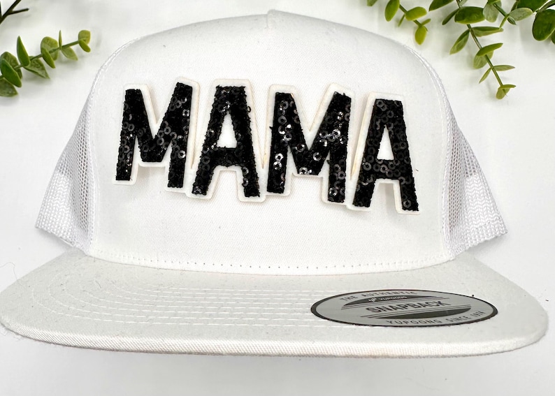 Op de afbeelding: Witte truckercap met een zwarte 'MAMA' patch van pailletten op de voorkant.