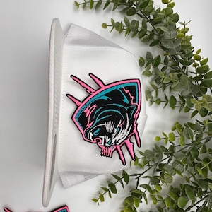 May include: White mesh baseball cap with a pink and blue embroidered panther patch. The patch features a panther with sharp claws and a fierce expression.