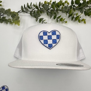 May include: White trucker hat with a blue and white checkered heart patch. The patch is made of glitter fabric.
