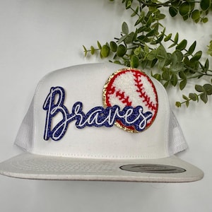 May include: White baseball cap with a blue and white "Braves" logo and a red and white baseball graphic.