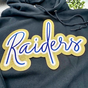 May include: Black hoodie with a gold and blue embroidered patch that says "Raiders".
