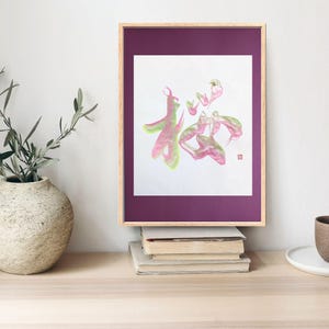Könnte beinhalten: Ein gerahmter Druck eines japanischen Kalligraphie-Kunstwerks in rosa und grünen Farbtönen. Die Kalligraphie ist das Wort "Hoffnung" auf Japanisch. Der Rahmen ist aus dunkelviolettem Holz mit einem weißen Passepartout.
