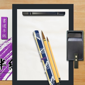 Può includere: Un set per calligrafia composto da una cartellina nera con fogli bianchi, due pennelli con manico giallo, un astuccio arrotolabile blu e bianco, una pietra per inchiostro nera con bastoncino marcato 書道 e una confezione di carta viola.