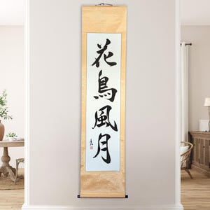 May include: A vertical scroll with Japanese calligraphy in black ink on a white background. The scroll is framed by a light wood border. The calligraphy reads "Flower, Bird, Wind, Moon".