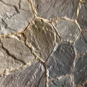 May include: A close-up of a stone wall with irregularly shaped stones. The stones are a mix of grey and brown colours. The mortar between the stones is a light brown colour.