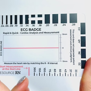 May include: A white plastic card with a red line and black markings. The card is labeled "ECG Badge" and "Rapid & Quick - Cardiac Analysis and Measurement". The card has a scale for measuring heart rate in beats per minute (bpm).