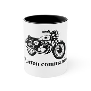 May include: A white ceramic mug with a black rim features a black and white illustration of a Norton Commando motorcycle. The text "Norton Commando" is printed in black below the motorcycle.