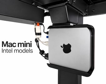 May include: A silver Mac mini computer mounted in a black under-desk bracket. The device features a black Apple logo on its side and is connected to various white and black cables. The text "Mac mini Intel models" is printed in black on the left.
