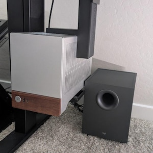 May include: A silver and brown computer tower mounted under a black desk with a black subwoofer on the floor.