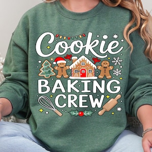 May include: Dark green sweatshirt with the text "Cookie Baking Crew" in white. The graphic includes a gingerbread house, gingerbread men, a Christmas tree, snowflakes, a whisk, and a rolling pin. The sweatshirt is heather dark green.